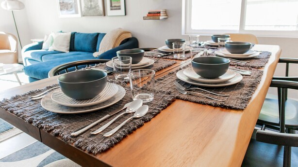 A dining table set with bowls, plates, glasses, and cutlery, with a blue sofa and books in the background. - Two-story mountain view retreat with two primary suites & ideal layout (Flagstaff)