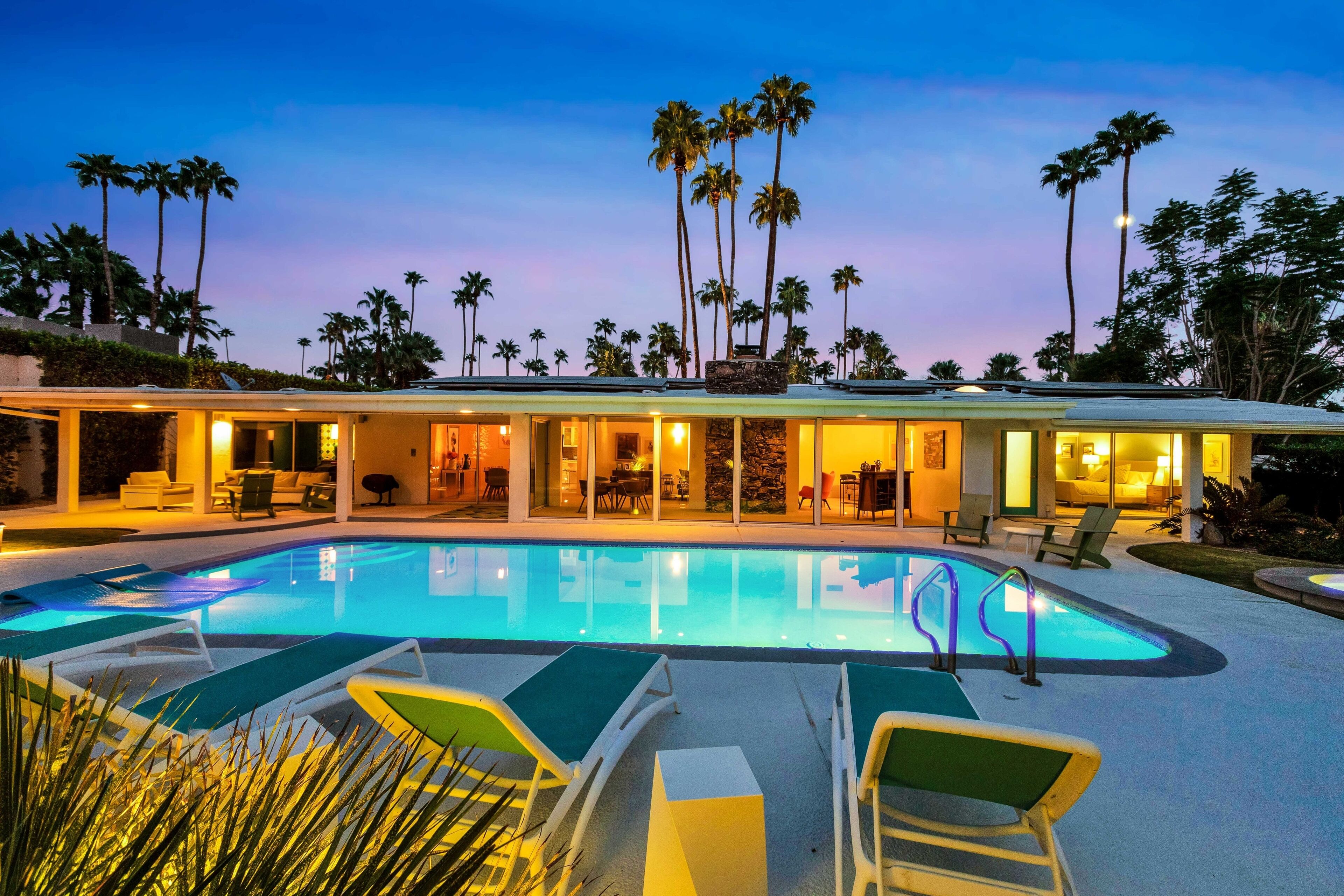 A poolside area with lounge chairs, a swimming pool, and a building with multiple rooms and a patio.