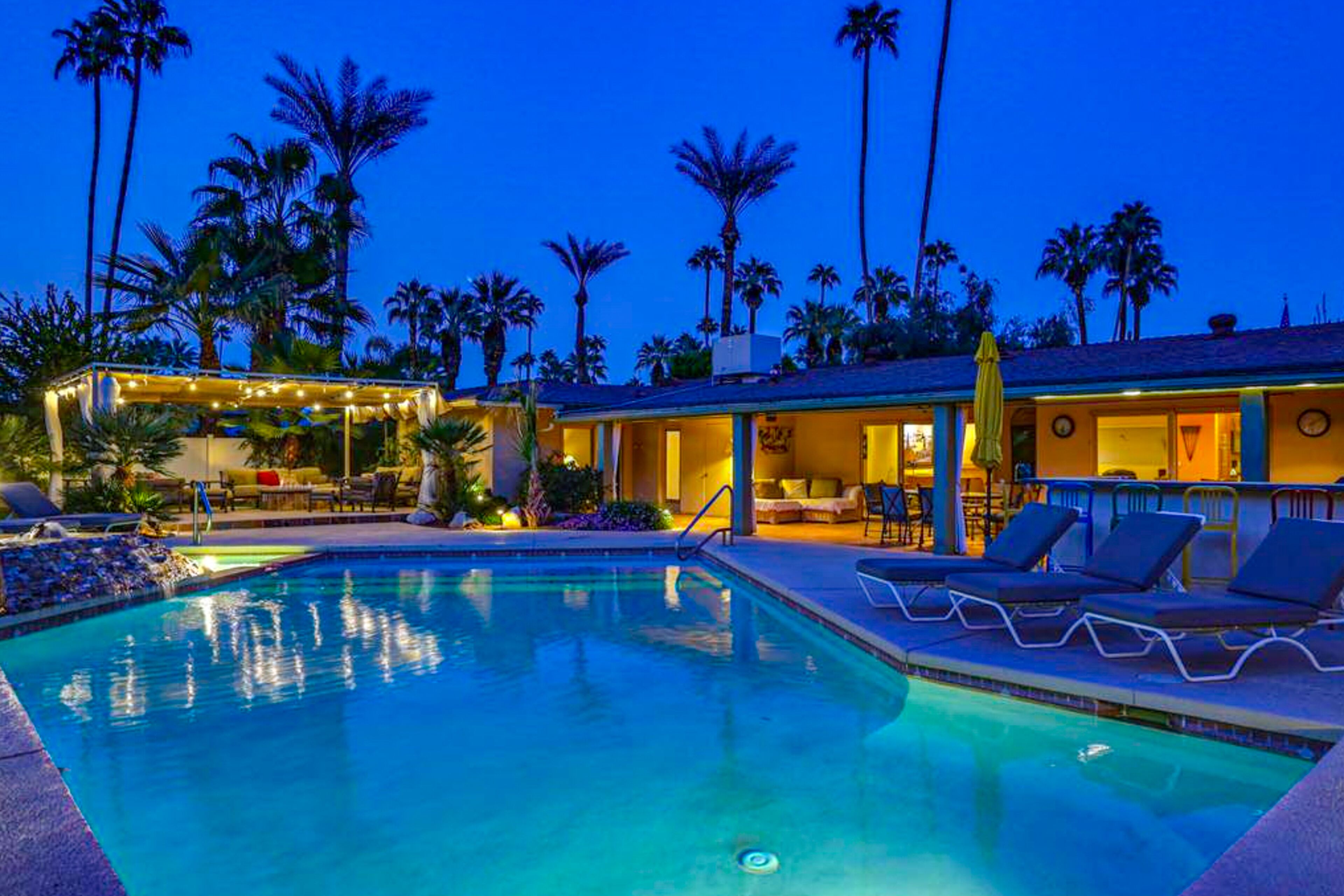 A pool area with lounge chairs and a covered seating area, surrounded by palm trees.