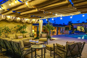 An outdoor lounge area with a pool, seating arrangements, and ambient lighting. - Spacious & luxurious dog-friendly home w/private pool spa & outdoor heated pool (Palm Springs)