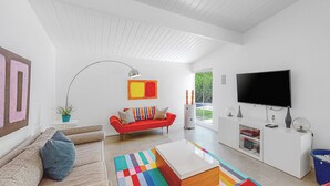 A modern living room with a red sofa, a white entertainment unit, and a flat-screen TV. - Sophisticated & modern home w/private gas grill, heated outdoor pool, large lawn (Palm Springs)