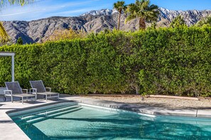 A swimming pool with lounge chairs, a hedge, and a mountain backdrop. - Sophisticated & modern home w/private gas grill, heated outdoor pool, large lawn (Palm Springs)
