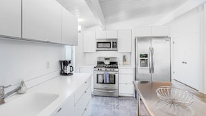 A modern kitchen with white cabinetry, stainless steel appliances, and a sleek countertop. - Sophisticated & modern home w/private gas grill, heated outdoor pool, large lawn (Palm Springs)