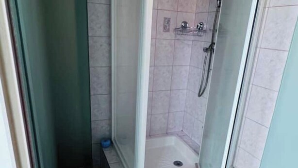 A glass-enclosed shower stall with a tiled floor and a small shelf above the showerhead. - Accommodation - Communay guest house. (Communay)