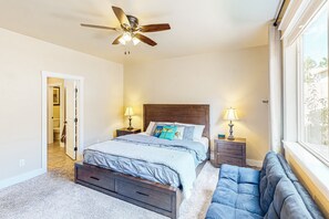 A bedroom with a bed, two bedside tables, a ceiling fan, a window, and a door leading to another room. - Stylish all-season home with dog-friendly yard, patio, central AC & washer/dryer (Flagstaff)