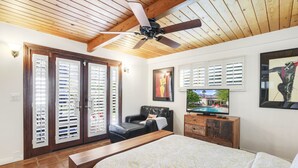 Ein Schlafzimmer mit einem großen Bett, einem Deckenventilator, einem Fernseher und Blick auf einen Swimmingpool durch das Fenster.