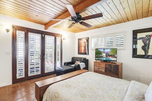 Ein Schlafzimmer mit einem großen Bett, einem Deckenventilator, einem Fernseher und Blick auf einen Swimmingpool durch das Fenster.