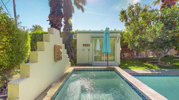 Ein Pool mit einer gefliesten Kante, eine kleine Struktur mit Tür und Handtuch, und im Hintergrund Palmen.