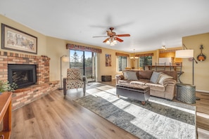 A living room with a fireplace, a ceiling fan, a sofa, and a coffee table. - Placid home with new fireplace, full kitchen, gas grill, patio, & washer/dryer (Flagstaff)