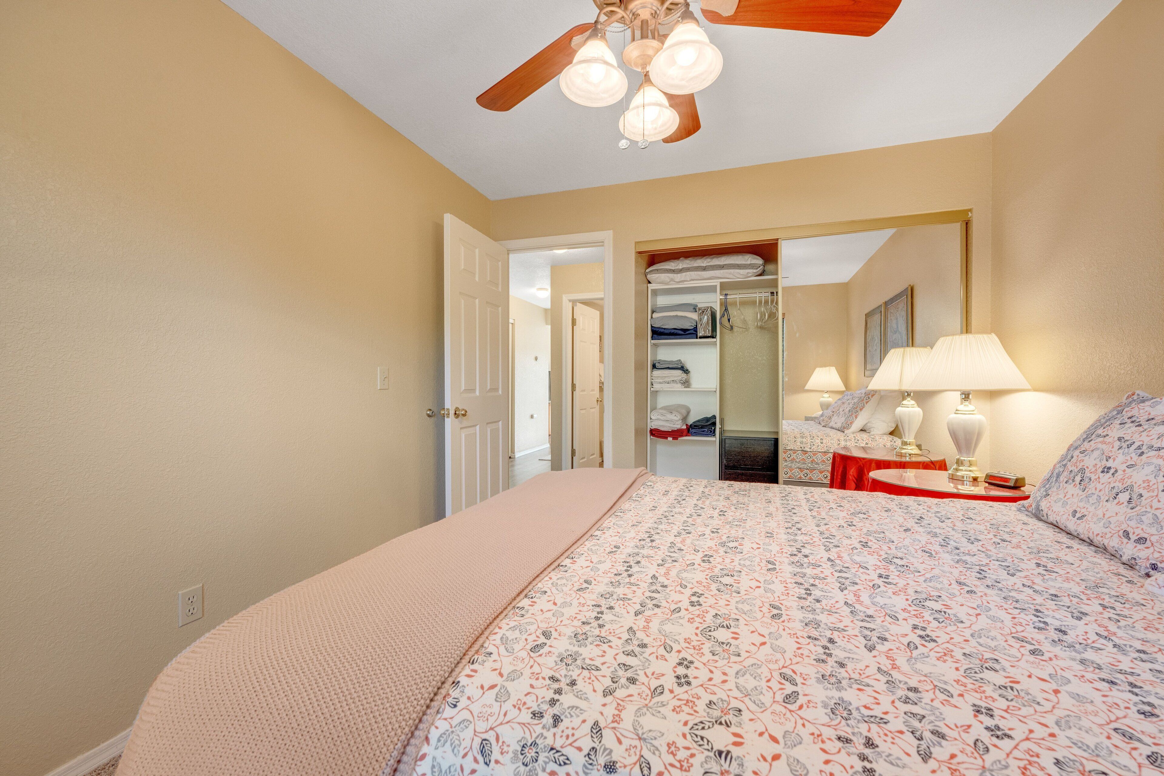 Une chambre à coucher comprenant un lit, un ventilateur de plafond, une table de chevet, une lampe et une armoire avec un miroir.