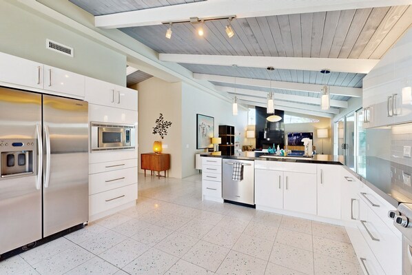 A modern kitchen with stainless steel appliances, white cabinetry, and a wooden ceiling. - Completely-updated, family-friendly home w/ private pool and spa (Palm Springs)