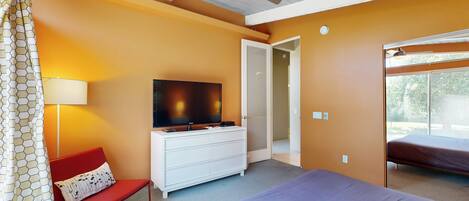 A hotel room with a bed, a TV on a white dresser, a red chair, and a ceiling fan.
