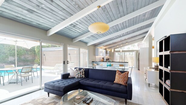 Un salon moderne avec une table basse en verre, des canapés sombres et une grande fenêtre donnant sur une piscine.