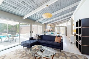 A modern living room with a glass coffee table, dark sofas, and a large window overlooking a pool. - Completely-updated, family-friendly home w/ private pool and spa (Palm Springs)