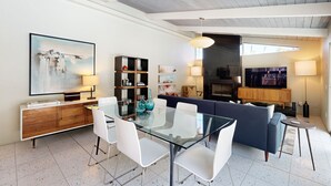 Un salon moderne avec une table à manger en verre, des chaises blanches, un canapé bleu et un téléviseur.