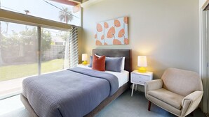 Une chambre moderne avec un grand lit, une table de chevet, une chaise et une fenêtre donnant sur l’extérieur.