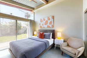A bedroom with a large bed, a nightstand with a lamp, a chair, and a wall art piece. - Completely-updated, family-friendly home w/ private pool and spa (Palm Springs)