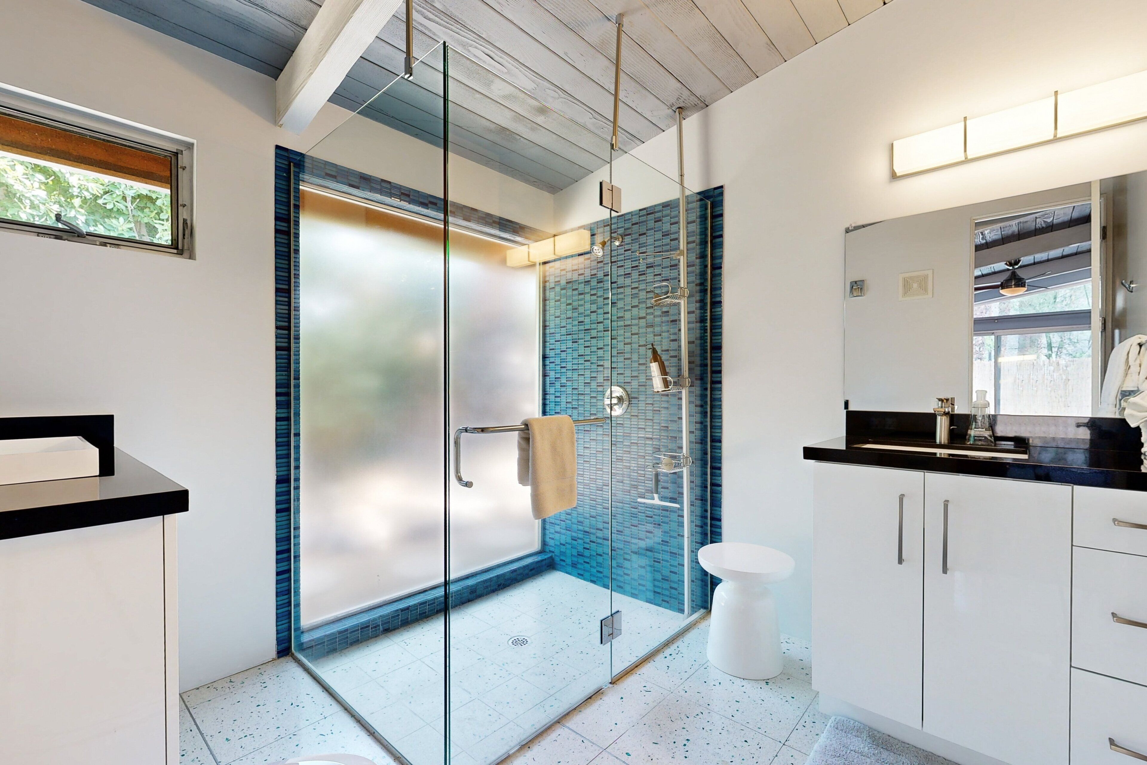 A modern bathroom with a glass shower enclosure, white cabinetry, and a large mirror.