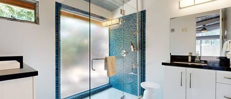 A modern bathroom with a glass shower enclosure, white cabinetry, and a large mirror.