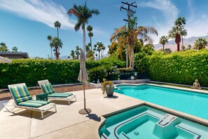 Un área de piscina con sillones de descanso, jacuzzi y palmeras.