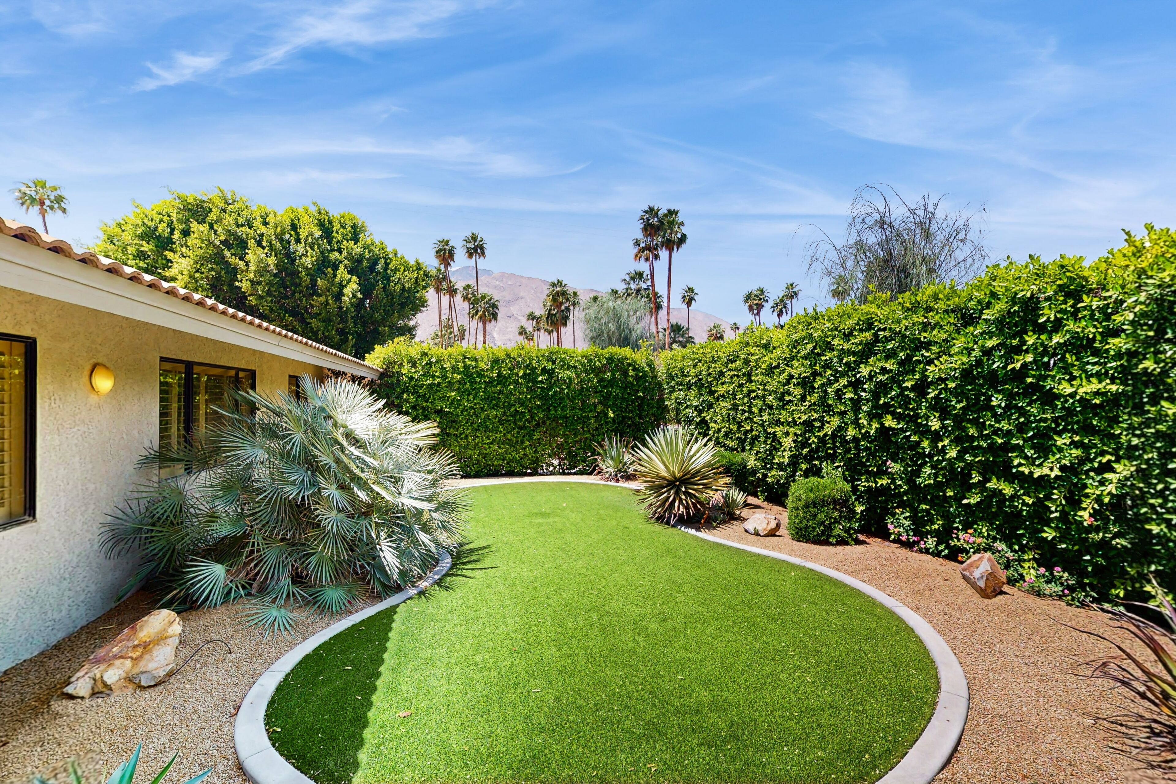 A well-maintained garden with a curved lawn, various shrubs, and a building with a tiled roof.