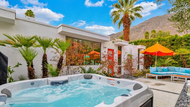 A hot tub with a view of a white building, outdoor seating, and palm trees. - Mid-century modern estate with a pool, hot tub, gourmet kitchen, and fireplace (Palm Springs)