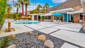 A pool area with lounge chairs, umbrellas, and a stone building. - Mid-century modern estate with a pool, hot tub, gourmet kitchen, and fireplace (Palm Springs)