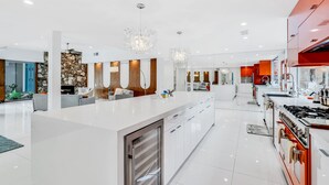 A modern kitchen with a central island, stainless steel appliances, and a red accent wall. - Mid-century modern estate with a pool, hot tub, gourmet kitchen, and fireplace (Palm Springs)