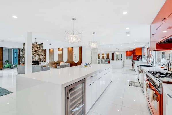 A modern kitchen with a central island, stainless steel appliances, and a red accent wall. - Mid-century modern estate with a pool, hot tub, gourmet kitchen, and fireplace (Palm Springs)
