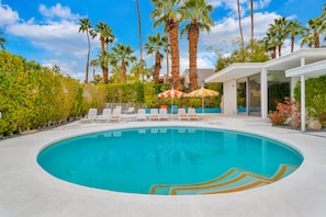 A swimming pool surrounded by palm trees and lounge chairs. - Mid-century modern estate with a pool, hot tub, gourmet kitchen, and fireplace (Palm Springs)