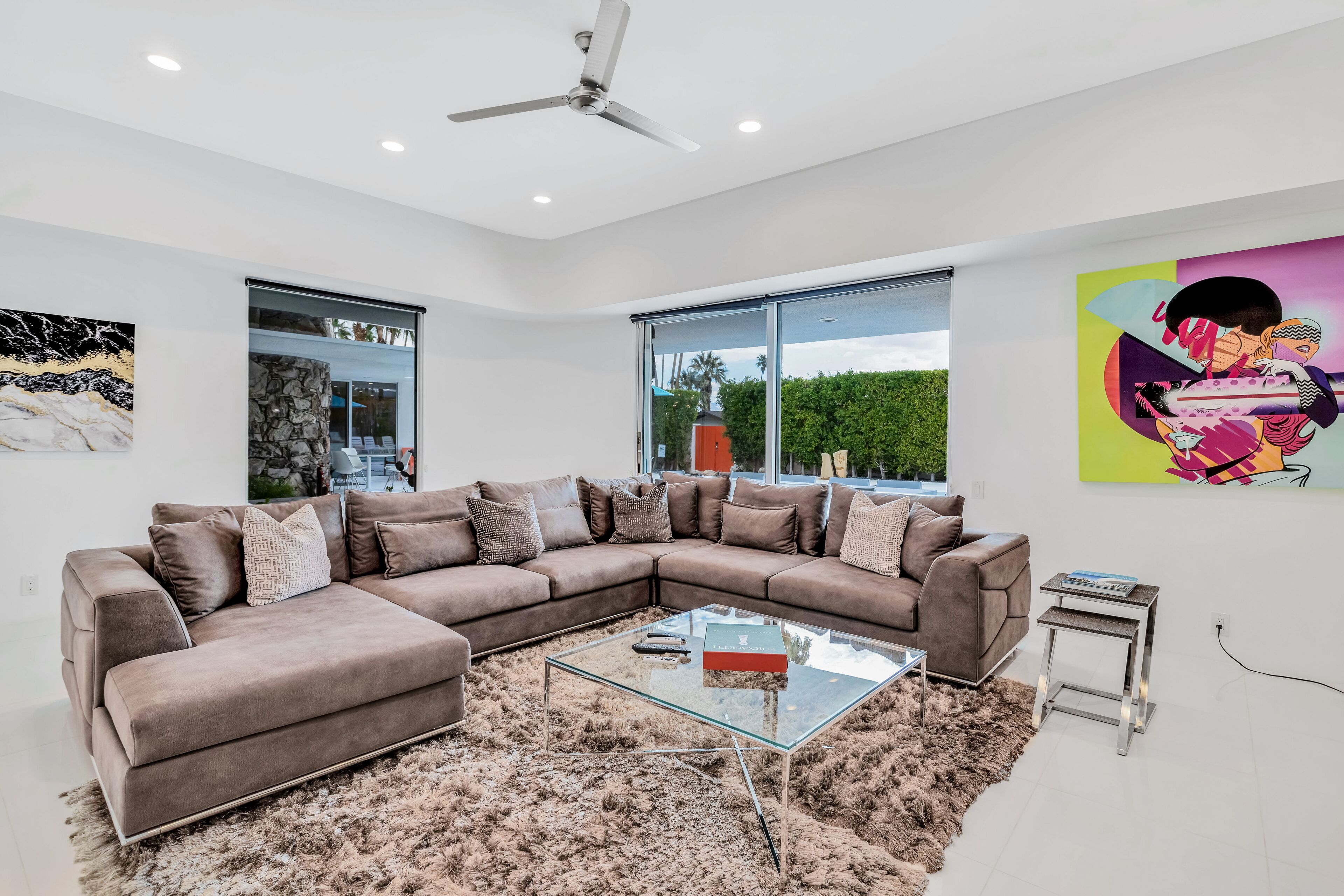A modern living room with a sectional sofa, a glass coffee table, and a large window offering a view of greenery.