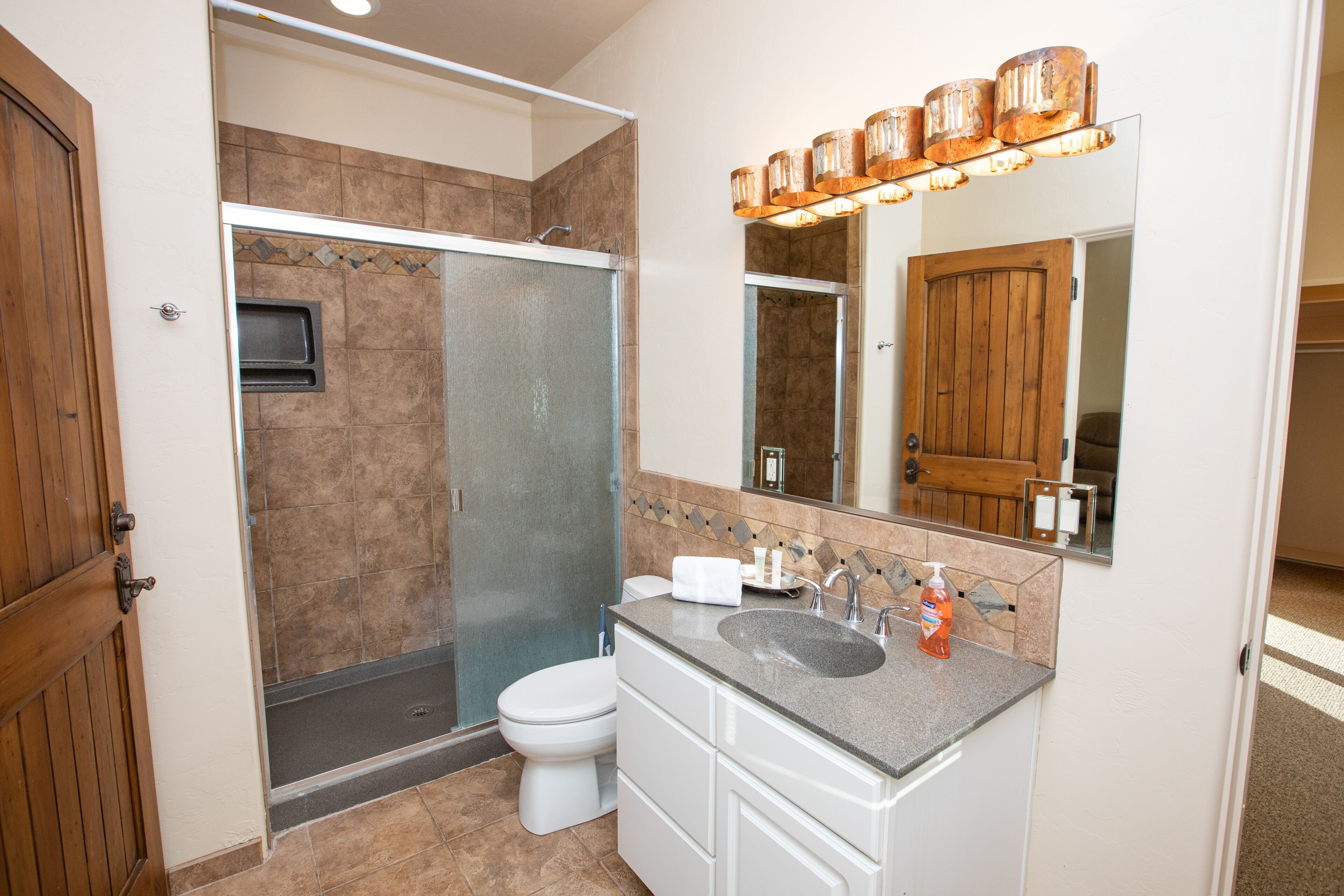 A bathroom with a shower, toilet, sink, and mirror.