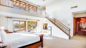 A spacious bedroom with a large bed, a balcony, and a staircase leading to an upper level. - Tucson ranch home with private pool, hot tub, gourmet kitchen, & patio (Marana)