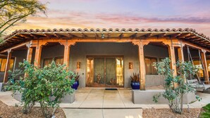 A traditional building with a tiled roof, a wooden porch, and a large glass door. There are potted plants on either side of the entrance. - Tucson ranch home with private pool, hot tub, gourmet kitchen, & patio (Marana)