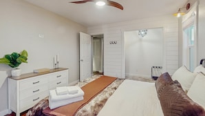 Une chambre à coucher comprenant un lit, une commode, un ventilateur de plafond et une porte donnant sur une autre pièce.
