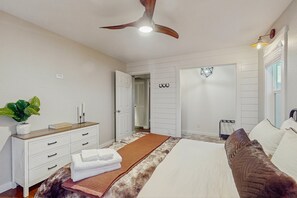 Un dormitorio con cama, cómoda, ventilador de techo y puerta que da a otra habitación.