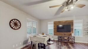 Un coin repas avec une table dressée pour quatre personnes, un ventilateur de plafond et un téléviseur fixé au mur.