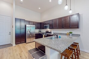 A modern kitchen with dark wood cabinets, stainless steel appliances, a granite countertop, and a bar stool. - Elegant home with mountain views, fireplace & grill (Flagstaff)