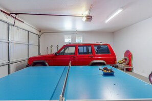 Eine Garage mit einem roten Fahrzeug, einem Tischtennis-Tisch und einem kleinen Tisch mit einer Schale Obst.