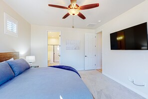 Ein Schlafzimmer mit Bett, Deckenventilator, Fernseher und einer Tür zu einem Badezimmer.