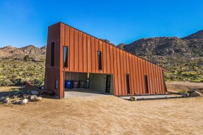 A modern, single-story building with a sloped roof, large windows, and a flat entrance area. - Desert stunner in Joshua Tree with mountain view - near town & park entrance (Joshua Tree)