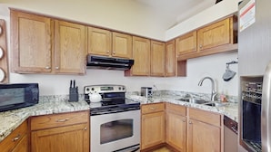 Una cocina con armarios de madera, horno de acero inoxidable, microondas, pileta y lavavajillas.