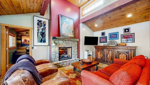 A cozy living room with leather sofas, a stone fireplace, and artwork on the walls.
