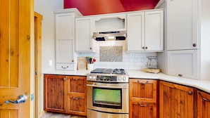 A kitchen with white cabinets, wooden lower cabinets, a stainless steel stove, and a tiled backsplash.