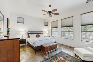 A bedroom with a bed, bedside tables, a nightstand, a ceiling fan, a wooden chest, and large windows. - Beautiful contemporary home with gorgeous views, private pool, & gas grill (Marana)