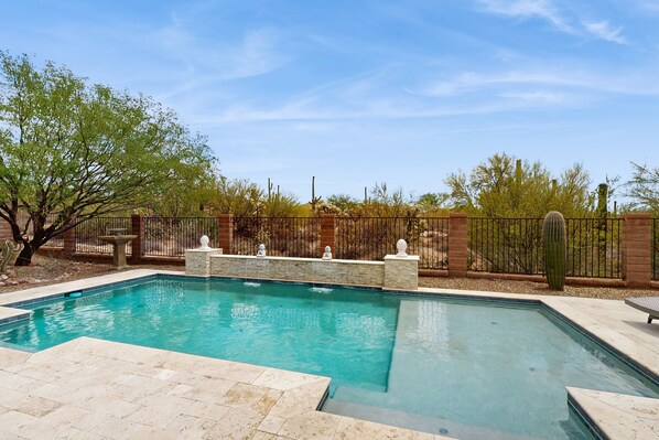 A rectangular swimming pool with a stone border, surrounded by a brick wall and a metal fence. - Beautiful contemporary home with gorgeous views, private pool, & gas grill (Marana)