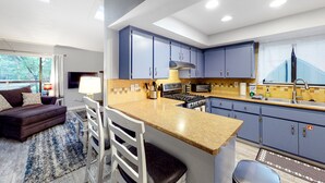 Una cucina moderna con mobili blu, un'isola centrale e una zona pranzo con divano e sedie.