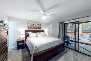 A bedroom with a large bed, a nightstand, a dresser, a ceiling fan, and a sliding glass door leading to an outdoor patio.