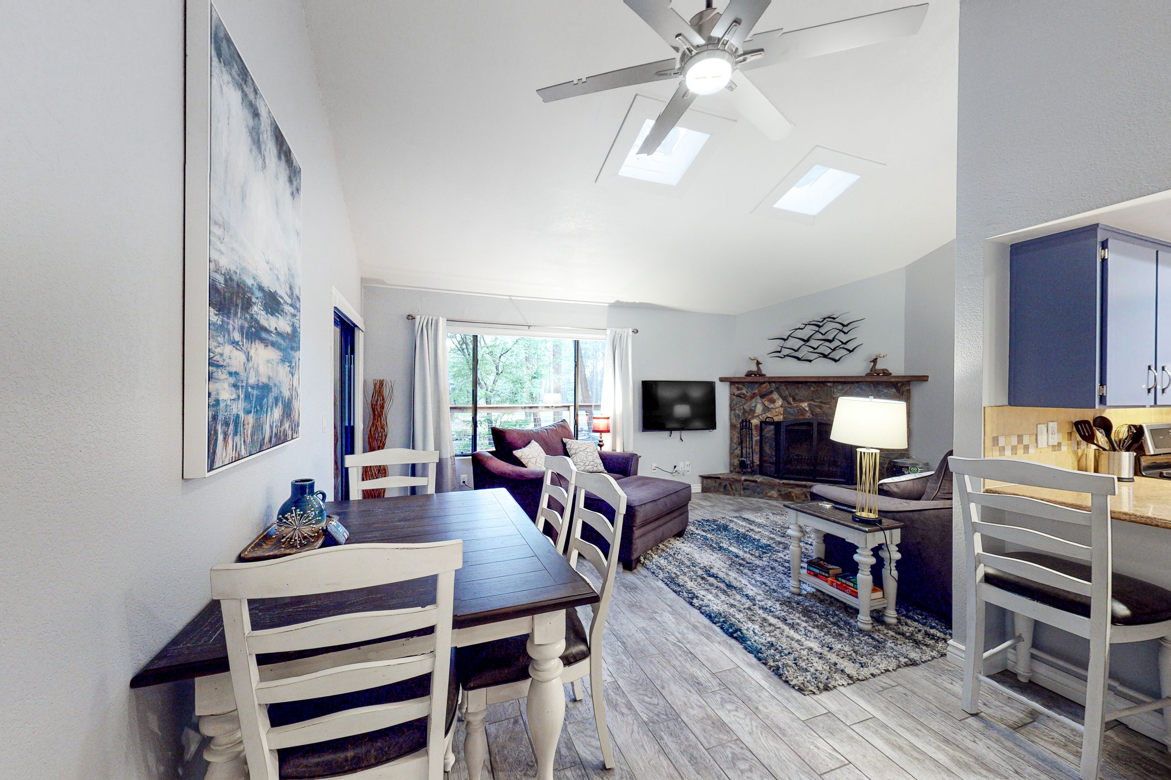 A modern living room with a dining area, a ceiling fan, a fireplace, and a television mounted on the wall.