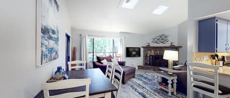 Un salon moderne comprenant un coin repas, un ventilateur de plafond, une cheminée et un téléviseur fixé au mur.